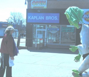 Sandy Spieler, HOBT Artistic Director, choreographs a MayDay Puppet”'s bow on Kaplan Bros. Plaza after Kaplan Bros. clothing store has “bowed-out” after 86 years. Kaplan Bros. and HOBT”'s Avalon Theatre are across the street from each other at Lake St. and 15th Ave. Harvey Winje